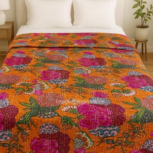 Może przedstawiać: Pomarańczowa kwiatowa kołdra z żywym wzorem różowych, niebieskich i zielonych kwiatów. Kołdra jest ułożona na łóżku z białymi prześcieradłami i poduszkami. Wzór kołdry ma szczegółowe przeszycia.