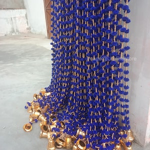 Könnte beinhalten: Eine blaue und goldene Dekor-Girlande mit Pompons und Glocken. Die Girlande ist aus blauem Samt und goldenen Perlen gefertigt. Die Glocken sind am unteren Ende der Girlande befestigt.