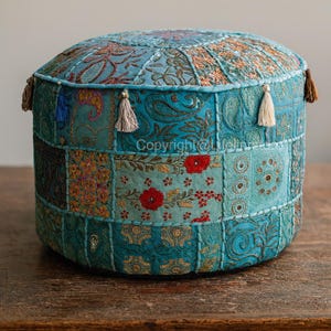 Può includere: Un pouf rotondo patchwork nei toni del verde acqua, turchese e oro. Il tessuto è decorato con motivi floreali e paisley, e i lati sono impreziositi da nappe. Un elemento decorativo per un soggiorno o una camera da letto.