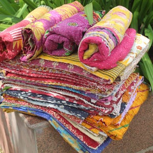 May include: A stack of colourful kantha quilts, made from recycled saris, with intricate patterns and textures. The quilts are folded and layered, creating a visually appealing display.
