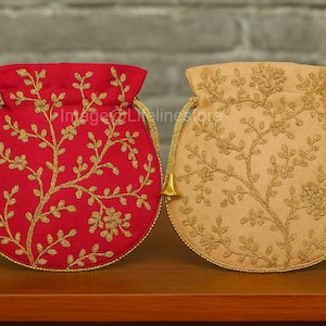 Puede incluir: Dos bolsos redondos con cordón, uno rojo y otro beige, ambos con bordados florales dorados. Tienen cordones y borlas doradas. Los bolsos se exhiben sobre una superficie de madera marrón.