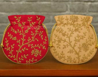 Könnte beinhalten: Zwei runde Beutel mit Kordelzug, einer rot und einer beige, beide mit goldenen Blumenstickereien. Sie haben goldene Kordelzüge und Quasten. Die Beutel werden auf einer braunen Holzoberfläche präsentiert.