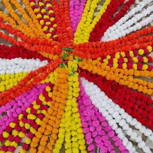 May include: A collection of colourful garlands made of artificial marigold flowers. The garlands are arranged in a circular pattern, with the colours radiating outwards from the centre. The colours include yellow, orange, red, pink, and white.