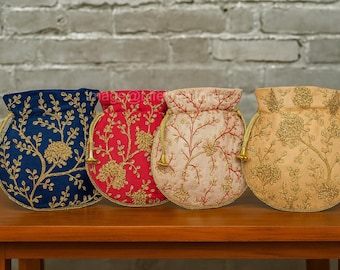 Könnte beinhalten: Vier bestickte Kordelzugbeutel in Marineblau, Rot, Creme und Gold. Jeder Beutel hat ein Blumendesign mit Goldfaden und einen passenden Kordelzugverschluss. Die Beutel werden auf einem Holztisch ausgestellt.