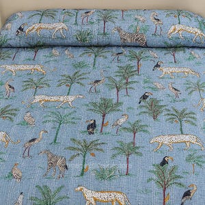 May include: A blue quilt featuring a safari theme with illustrations of leopards, zebras, toucans, ostriches, and palm trees. The design is repeated across the quilt's surface, creating a cohesive pattern. The quilt is likely made of soft fabric.