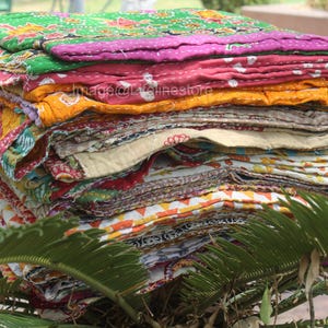 May include: A stack of colourful kantha quilts, made from recycled saris, with a variety of patterns and textures. The quilts are folded and stacked on top of each other, creating a visually appealing display.