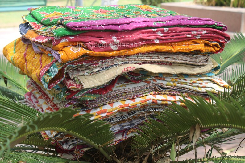 May include: A stack of colourful kantha quilts, made from recycled saris, with a variety of patterns and textures. The quilts are folded and stacked on top of each other, creating a visually appealing display.