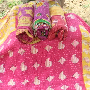 Può includere: Un quilt kantha rosa e giallo con un motivo paisley. Il quilt è piegato e arrotolato, con le estremità del tessuto visibili.