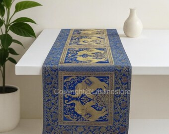 May include: A blue and gold table runner featuring an elephant motif. The runner is rectangular, adorned with gold elephants and floral patterns against a blue backdrop. The text "Copyright@Lifelinestore" is visible on the fabric.