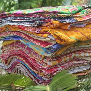 May include: A stack of colourful kantha quilts, made from recycled saris, with a variety of patterns and textures. The quilts are folded and stacked on top of each other, creating a visually appealing display.