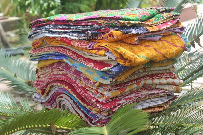 May include: A stack of colourful kantha quilts, made from recycled saris, with a variety of patterns and textures. The quilts are folded and stacked on top of each other, creating a visually appealing display.