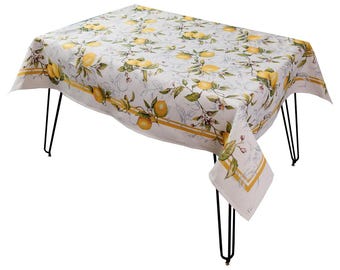 May include: A rectangular tablecloth with a lemon pattern. The white fabric features yellow lemons, green leaves, and small pink flowers. A yellow stripe borders the edge. The tablecloth is draped over a table with black metal legs.