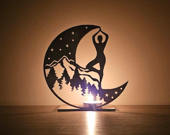 Peut inclure: Bougeoir en métal noir en forme de croissant de lune avec une scène de montagne et de forêt. Une silhouette d'une personne en posture de yoga est sur la montagne. Le bougeoir est sur une surface en bois.