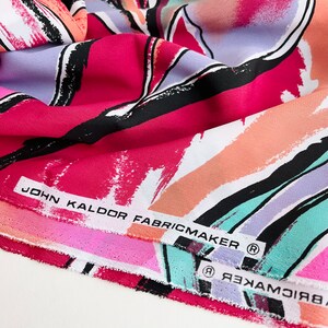 May include: Close-up of a folded fabric with an abstract print in shades of pink, orange, blue, and green. The fabric has a black and white brushstroke design. The label reads "John Kaldor Fabricmaker (R)".
