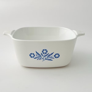 May include: White square casserole dish with blue floral design. The dish has two handles and a simple, elegant shape. The blue floral pattern is centered on the front of the dish.