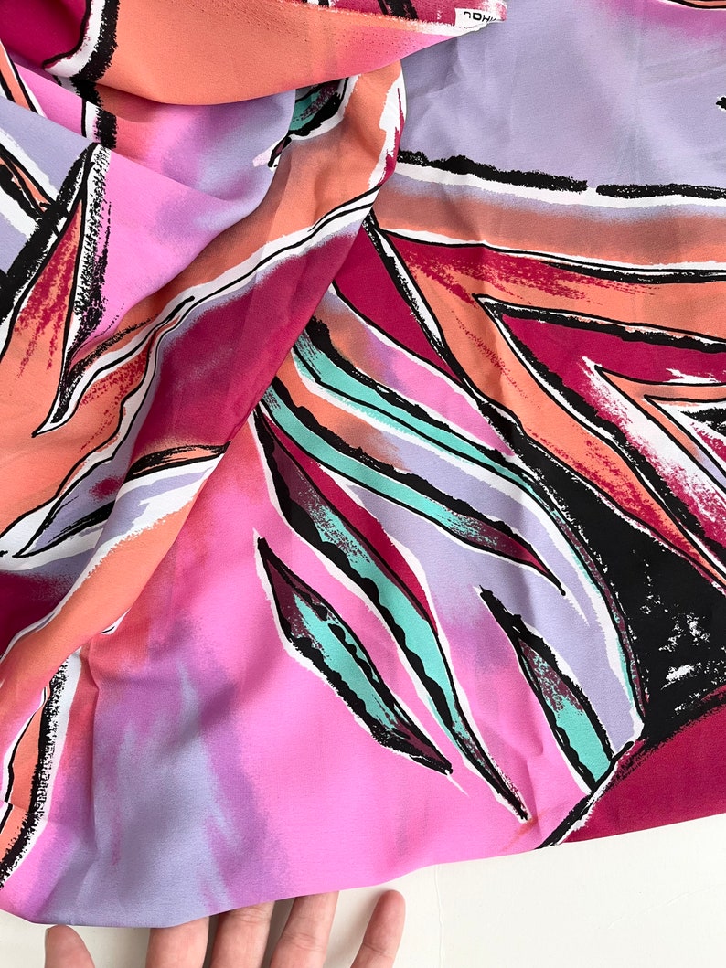 May include: A pink, purple, orange, and teal fabric with a geometric pattern of abstract leaves. The fabric is soft and flowing.