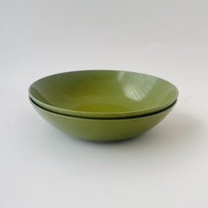 May include: Two olive green ceramic bowls stacked on top of each other. The bowls have a smooth, glossy finish and a simple, modern design. The bowls are empty and ready to be filled.