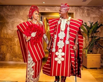 May include: A couple in traditional red and white striped clothing, with the woman holding a feathered fan. The man is holding a walking stick. They are smiling and looking at each other.
