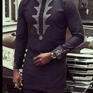 May include: A black long-sleeved shirt with a silver embroidered design on the front. The shirt has a mandarin collar and a button closure.