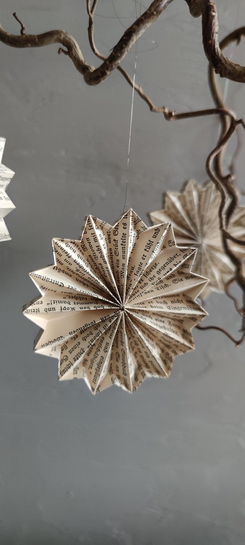 May include: Handmade paper star ornaments, crafted from vintage book pages. These unique decorations feature a starburst design, suspended by a thin string, and add a touch of rustic charm to any space.
