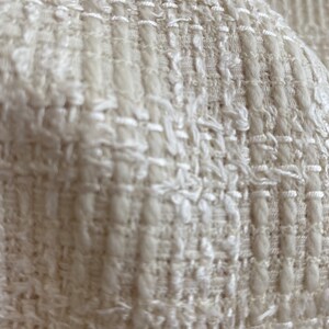 May include: Close-up of a white textured fabric with a woven pattern. The fabric has a soft, fluffy texture.