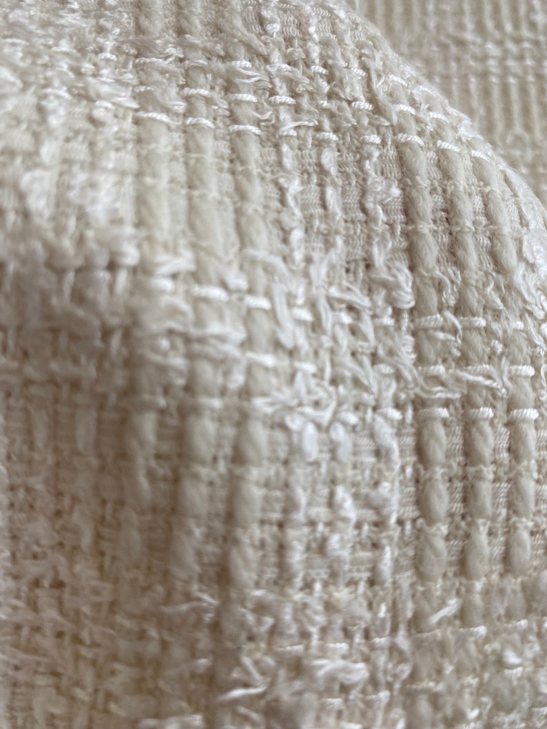 May include: Close-up of a white textured fabric with a woven pattern. The fabric has a soft, fluffy texture.