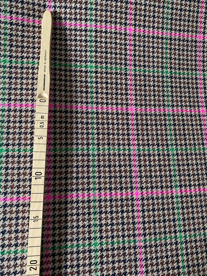 May include: Brown, black, and green houndstooth fabric with pink and green stripes. The fabric is measured with a ruler that shows 20 inches.