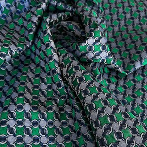 May include: A close-up shot of a fabric with a chain-link design. The fabric is a mix of green, grey, and navy blue. The material is likely intended for clothing or home furnishings.