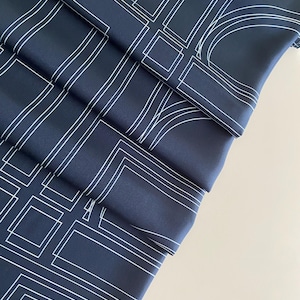 Könnte beinhalten: Marineblauer Stoff mit einem weißen geometrischen Muster aus Quadraten, Rechtecken und geschwungenen Linien. Der Stoff ist gefaltet, wodurch ein geschichteter Effekt entsteht. Das Design ist modern und abstrakt.