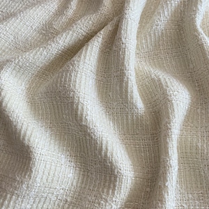 May include: Close-up of a white textured fabric with a woven pattern. The fabric is soft and has a slightly rough texture.