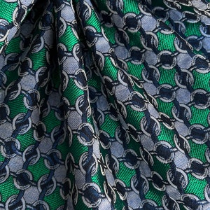 May include: Close-up of a fabric with a chain link pattern. The fabric features a repeating design of interlocking circles in shades of green, blue, and grey. The fabric is folded, showing texture and depth.