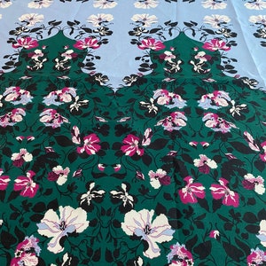 May include: A green fabric with a floral pattern. The flowers are white, pink, and blue. The fabric has a repeating pattern.