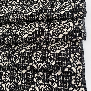May include: Black and white fabric with a repeating pattern of roses and a grid. The fabric has a textured surface.
