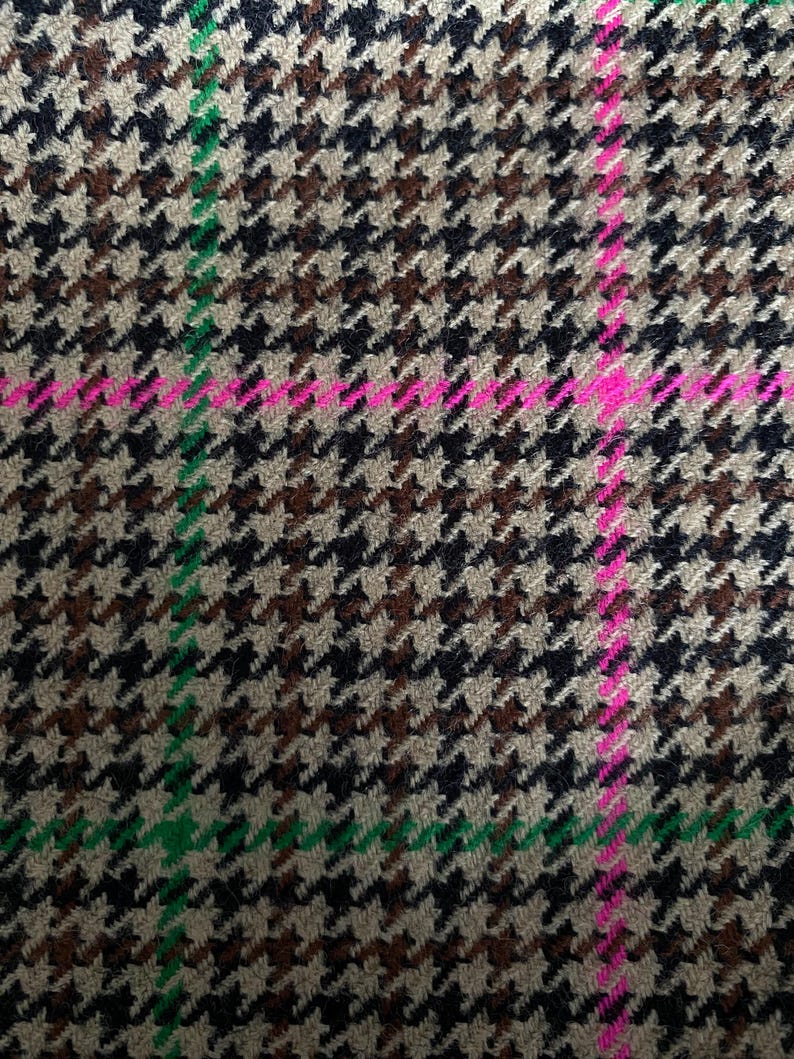 May include: A close-up of a brown, black, and white houndstooth fabric with a green and pink plaid pattern.