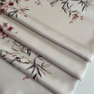 Könnte beinhalten: Gefalteter Stoff mit floralem Muster. Das Design zeigt rosa und rote Blüten mit grünen und grauen Blättern auf einem hellbeigen Hintergrund. Der Stoff ist in Schichten gefaltet und zeigt den detaillierten Druck.