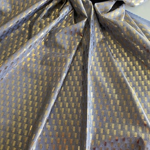 Puede incluir: Una tela azul con un patr&oacute;n geom&eacute;trico dorado. La tela est&aacute; tejida con un brillo sutil y tiene una textura suave y fluida.
