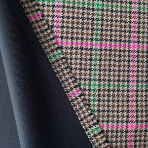 May include: Close-up of a brown and black houndstooth fabric with pink and green stripes. The fabric is folded over a black fabric.