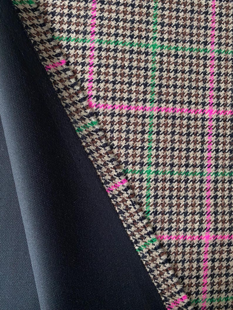 May include: Close-up of a brown and black houndstooth fabric with pink and green stripes. The fabric is folded over a black fabric.
