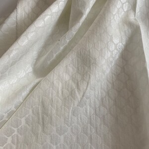 Puede incluir: Tela blanca con un sutil patr&oacute;n geom&eacute;trico en relieve. La tela tiene un tacto suave y lujoso.
