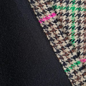 May include: Close-up of a black fabric with a brown, black, green, and pink houndstooth pattern fabric sewn on the diagonal.