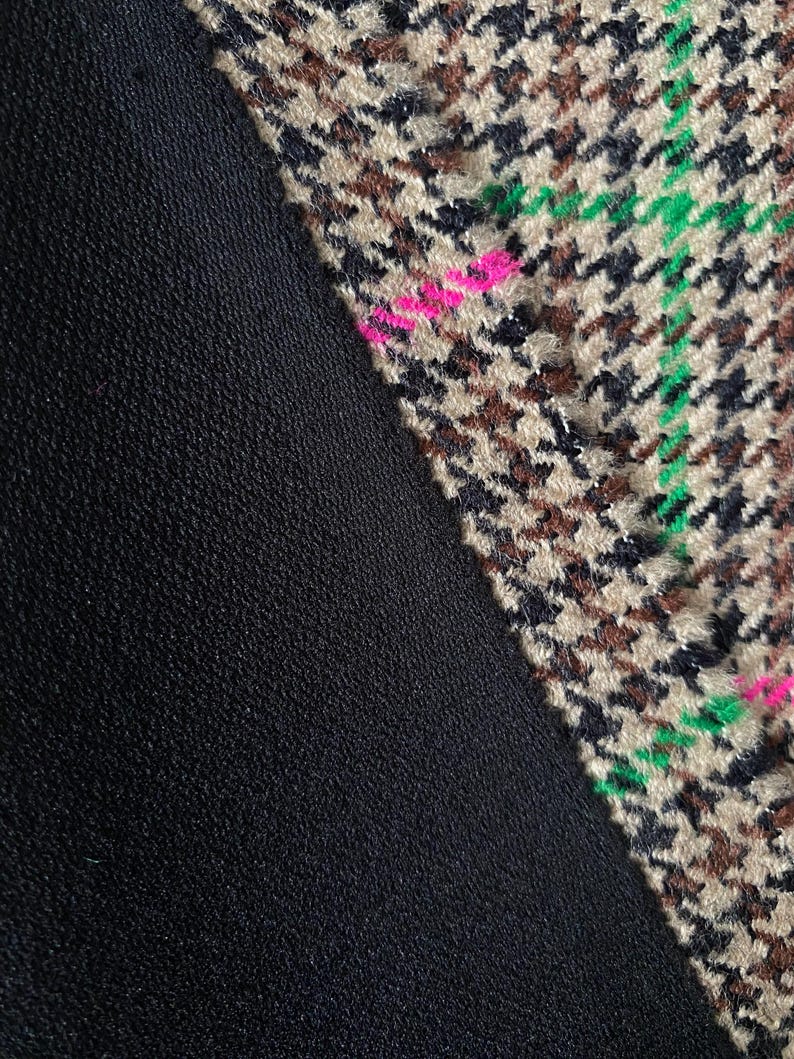 May include: Close-up of a black fabric with a brown, black, green, and pink houndstooth pattern fabric sewn on the diagonal.