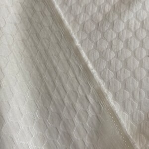 Puede incluir: Tela blanca con un patr&oacute;n geom&eacute;trico texturizado. La tela tiene un brillo sutil y una sensaci&oacute;n suave y lisa.