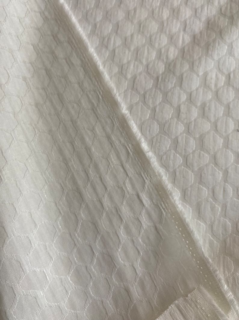 Puede incluir: Tela blanca con un patr&oacute;n geom&eacute;trico texturizado. La tela tiene un brillo sutil y una sensaci&oacute;n suave y lisa.