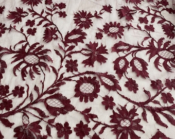 May include: Burgundy floral lace fabric with a scalloped edge. The lace has a delicate floral pattern and is perfect for adding a touch of elegance to any project.