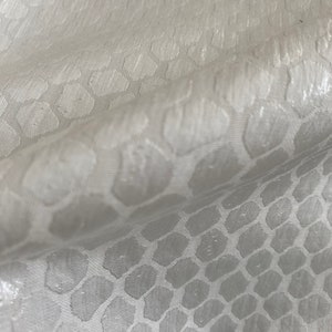 Puede incluir: Tela blanca con un sutil patr&oacute;n en relieve de formas hexagonales repetidas.