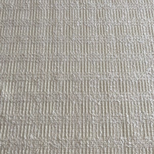 May include: Close-up of a white textured fabric with a woven pattern. The fabric has a slightly rough texture and a subtle sheen.