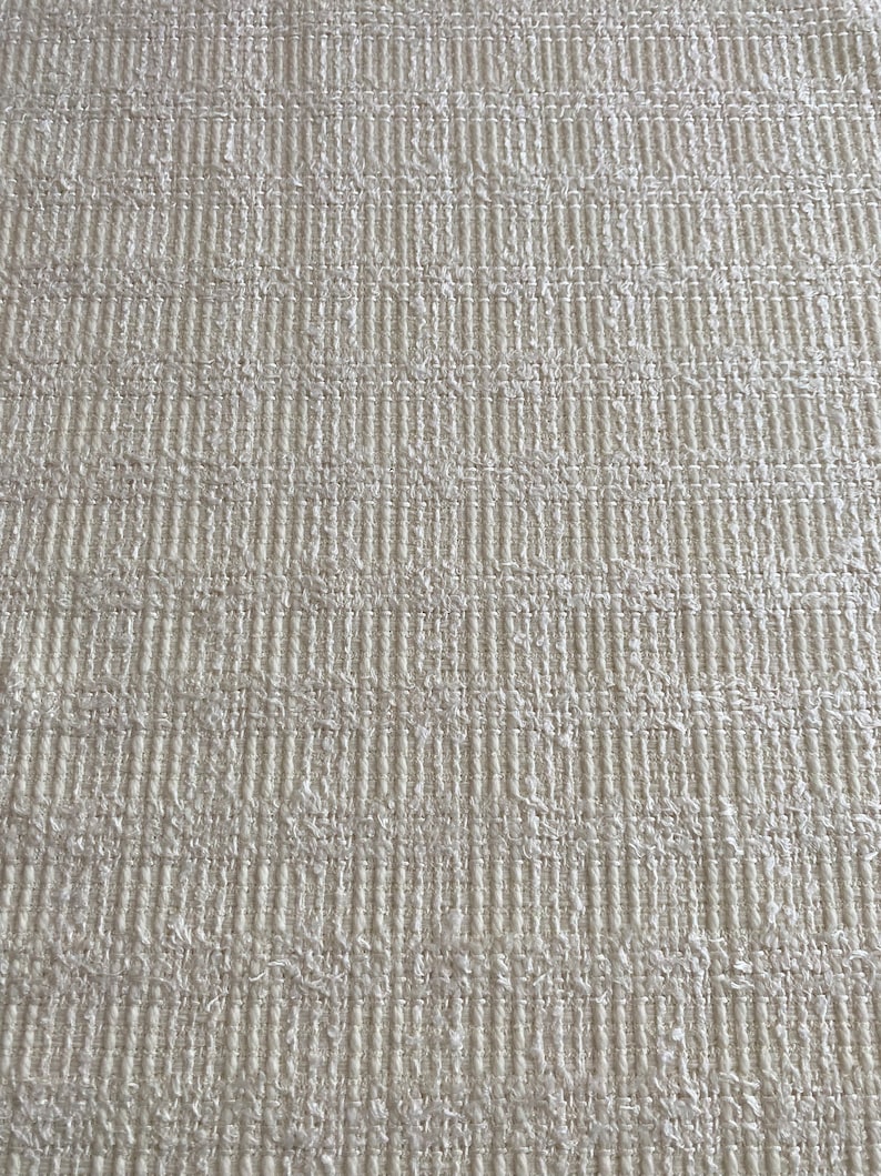 May include: Close-up of a white textured fabric with a woven pattern. The fabric has a slightly rough texture and a subtle sheen.
