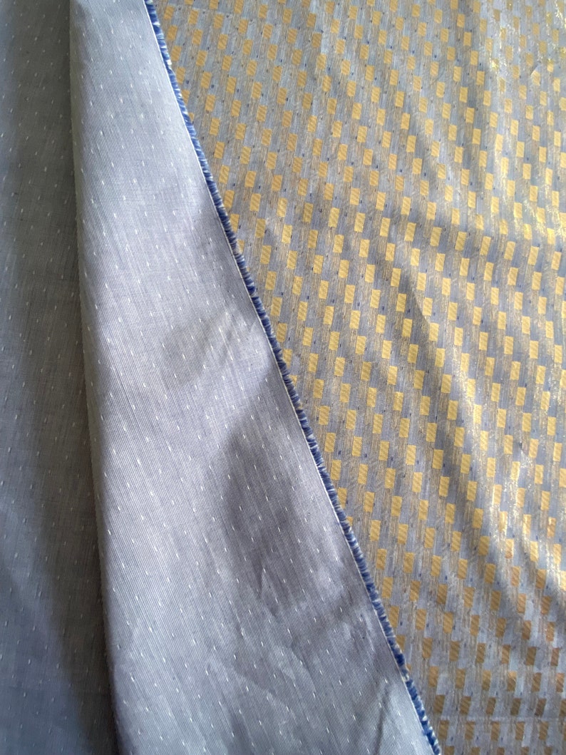 Puede incluir: Primer plano de dos telas, una es gris claro con una textura sutil y la otra es gris claro con un patr&oacute;n geom&eacute;trico dorado.