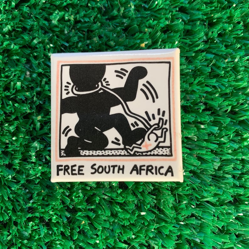Puede incluir: Pin cuadrado con un gr&aacute;fico en blanco y negro de una persona con una cuerda alrededor del cuello, extendiendo la mano. El texto "FREE SOUTH AFRICA" est&aacute; debajo. El pin tiene un fondo blanco con un borde rosa.