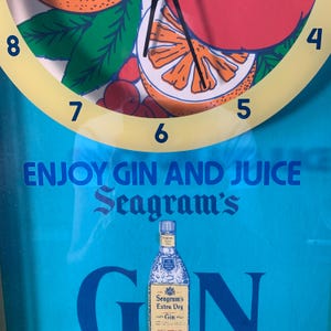 May include: A blue and yellow clock with a citrus fruit design. The clock face reads "Enjoy Gin and Juice Seagram's" and features a bottle of Seagram's Extra Dry Gin.